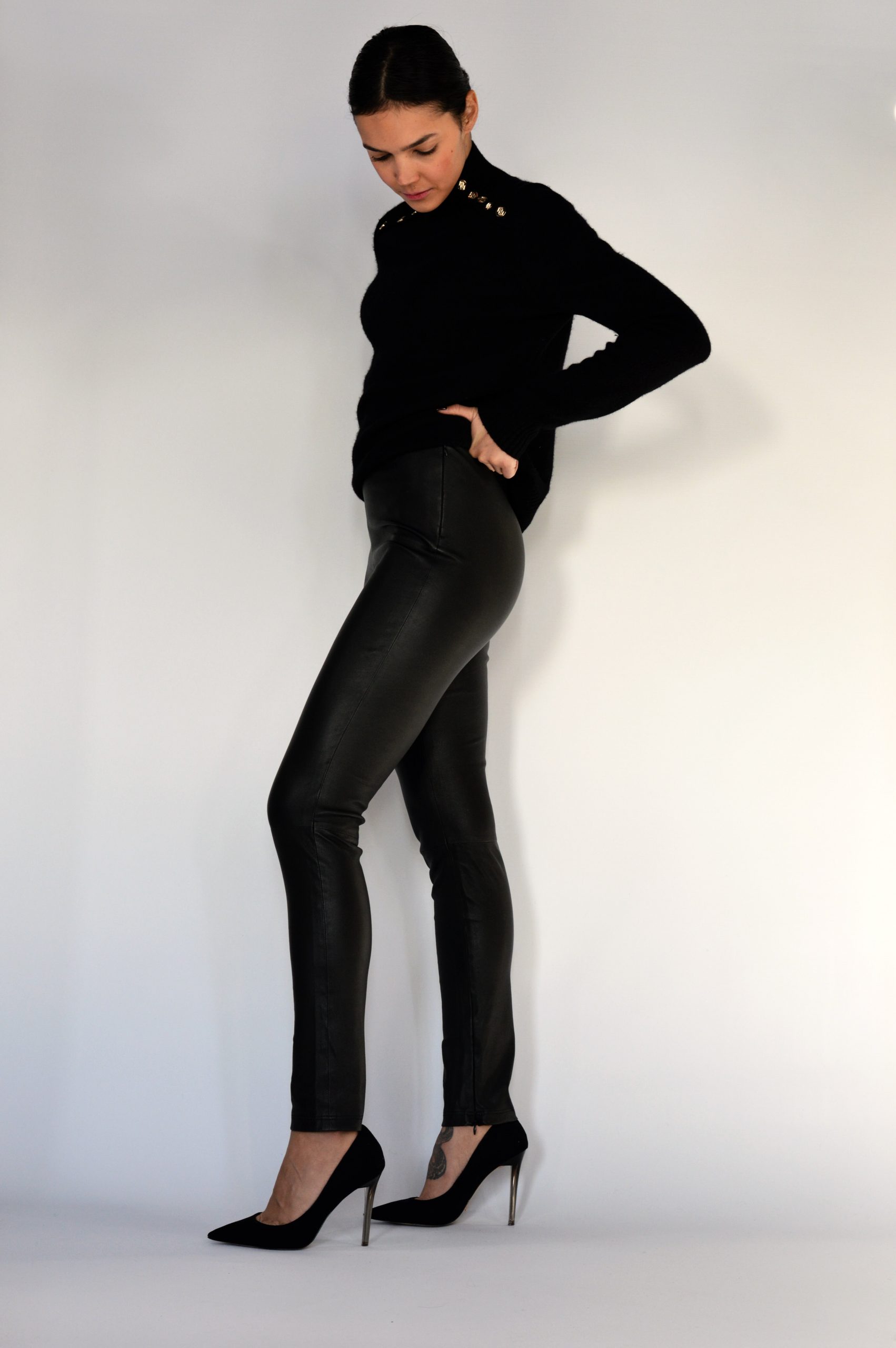 woman wearing black leather pants with a black top and high heels side view looking down
