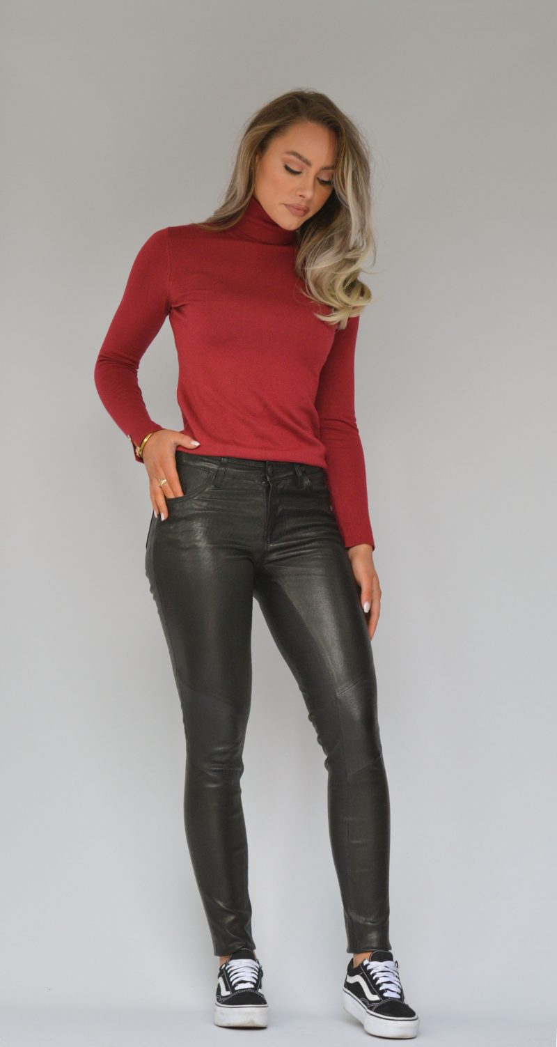 blond woman wearing black leather pants with red turtle neck and vans