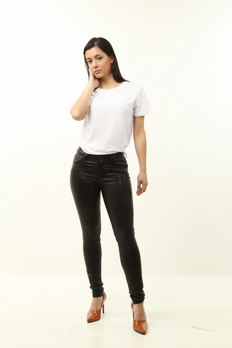 Woman wearing black leather pants on heels with a white shirt and white background