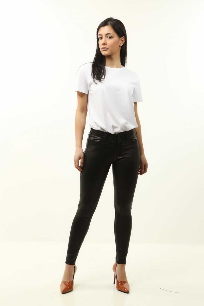 Woman wearing black leather pants on heels with a white shirt and white background